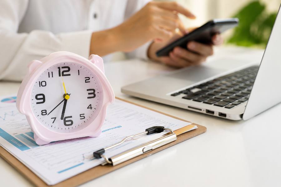 Alarm clock on desk with person using phone and laptop